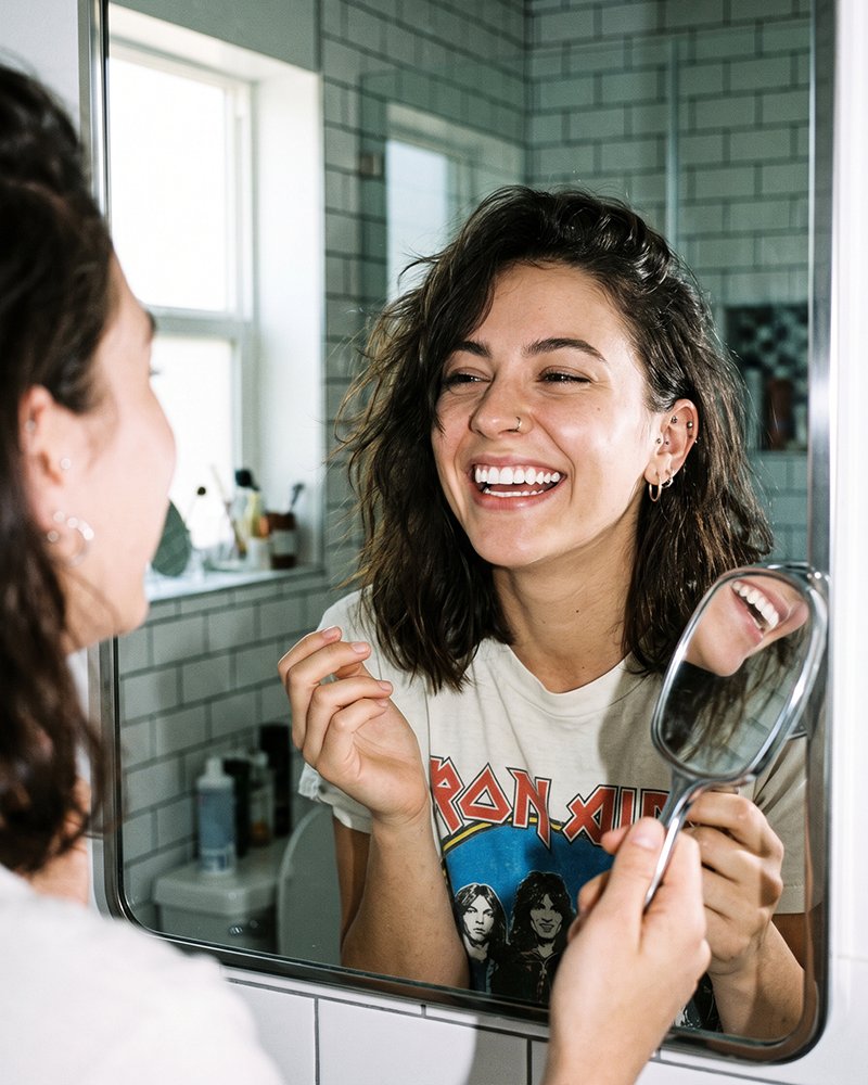 A patient laughing at her smile in the bathroom mirror
