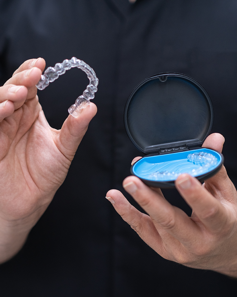 A clear aligner and its case, held up to the light